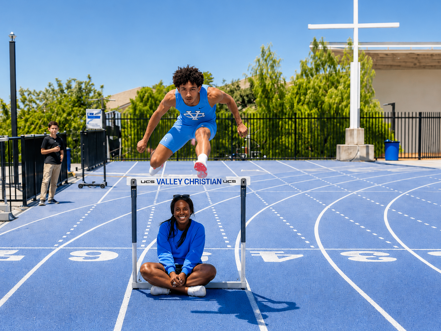Coach Jo with a high school hurdler clearing a hurdle on the track